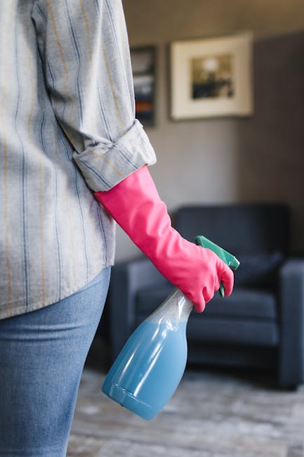 A person is carefully unrolling a beige and brown patterned carpet onto a polished wooden floor inside a residential living room. The carpet appears clean and well-maintained, with a soft texture visi
